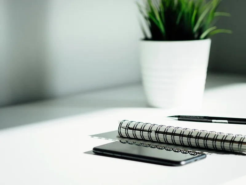 A blank notebook, pen and phone on a white desk